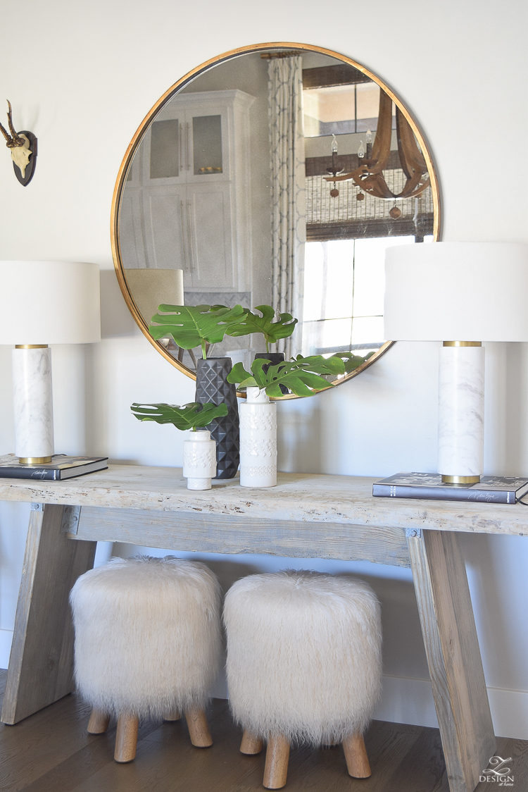 zdesign at home spring tour rustic console with round gold mirror fur stools philadendron branches white global inspired vases gray wood floors marble and brass lamps-1