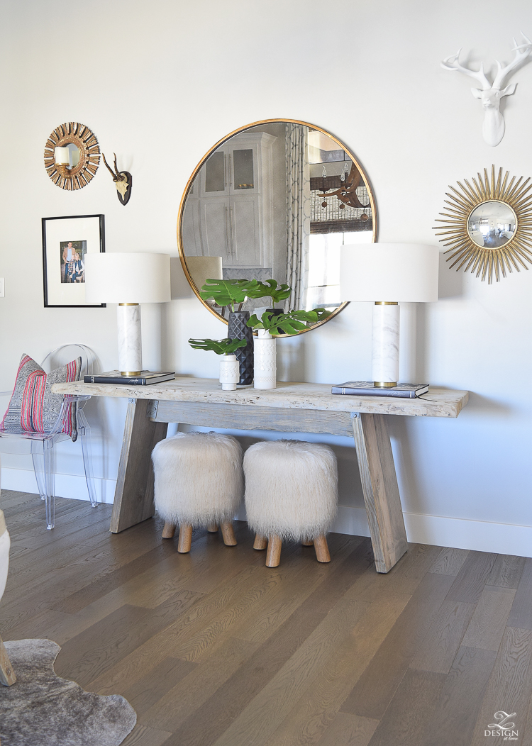 zdesign at home spring tour rustic console with round gold mirror fur stools philadendron branches white global inspired vases gray wood floors marble and brass lamps-2