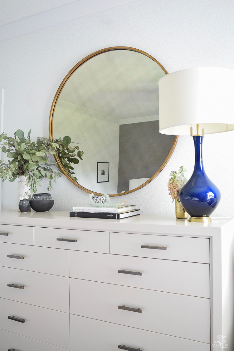 Transitional-modern-style-bedroom-decor-black-and-white-modern-vases-round-gold-mirror-navy-and-gold-lamp-modern-gray-dresser-with-brass-hardware-2.