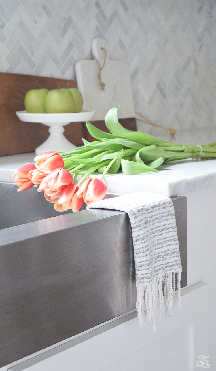https://www.zdesignathome.com/wp-content/uploads/2017/08/styling-and-decorating-the-kitchen-counters-fringe-dish-towel-tulips-and-flowers-in-the-sink-kohler-stainless-farmhouse-sink-1.jpg