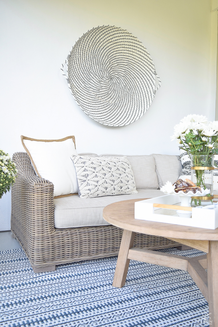 Outdoor fall patio with white mums and texture gray rattan outdoor sofa fringe and sequin pillows blue and white outdoor rug large wall hanging basket-1