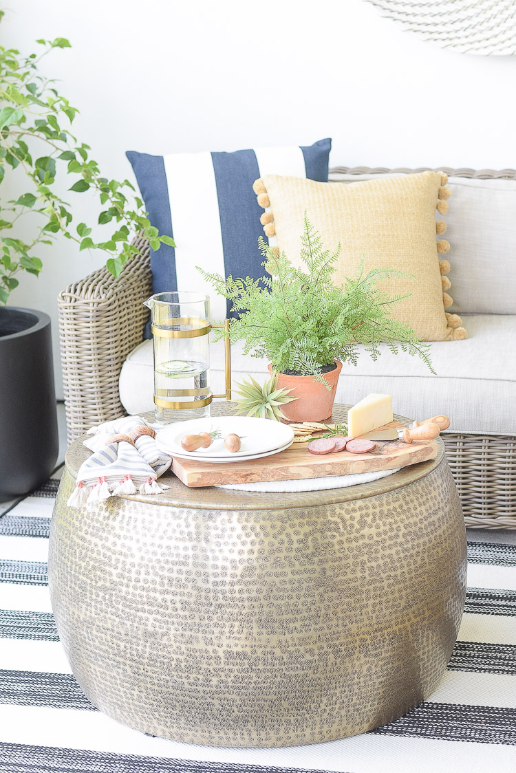 Sustainably sourced outdoor home decor - pillows, cheese board, round gold hammered coffee table, water pitcher