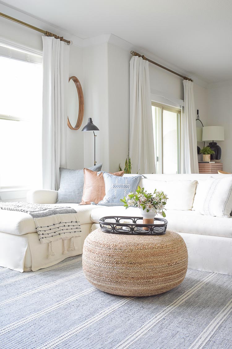 Spring Living Room Tour - round jute ottoman in boho chic living room with white sofa and curtains 