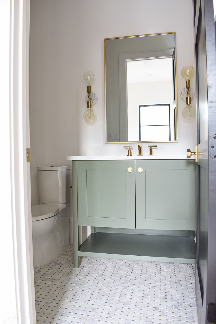 Bathroom with basketweave marble floors, green vanity and gold accents 