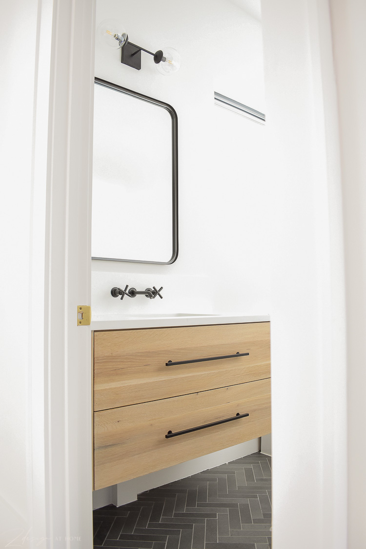 white oak floating cabinet in bathroom with black hardware, black faucet, black SM mirror and sconce 