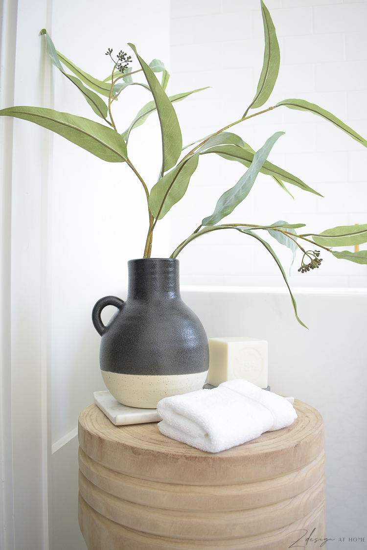 black two tone pottery vase with green stem on stool styled in front of tub - beautiful black and white modern bathroom 