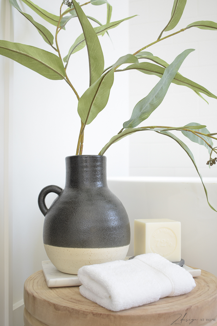 black two tone pottery piece with green stem styled in front of free standing tub 