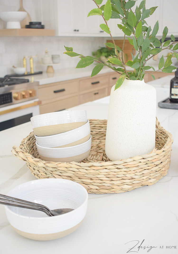 stoneware bowls, round rattan tray, speckled vase on kitchen island 