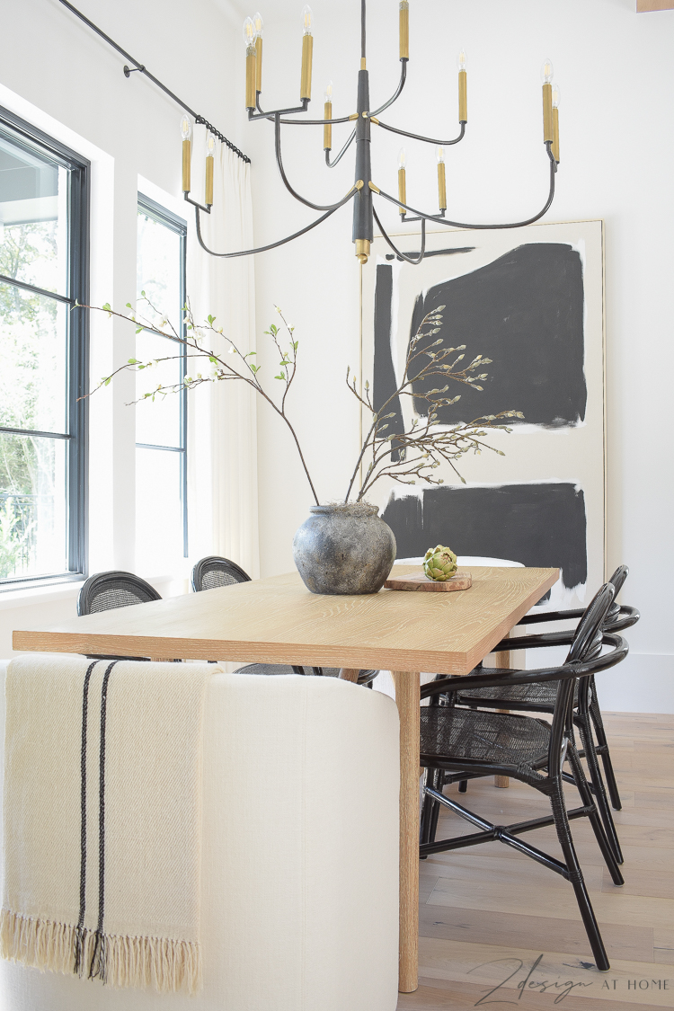 Modern farmhouse black and white themed dining room with black rattan dining chairs and oversized art, brass and black chandelier 