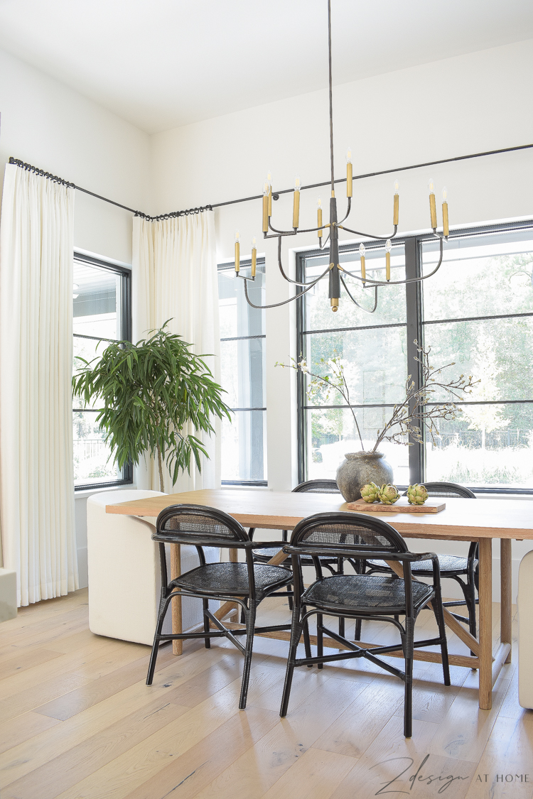 Modern farmhouse black and white themed dining room with black rattan dining chairs and oversized art, brass and black chandelier 