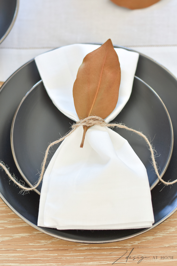 modern black dishes with white linen napkin and magnolia leaf attached with twine