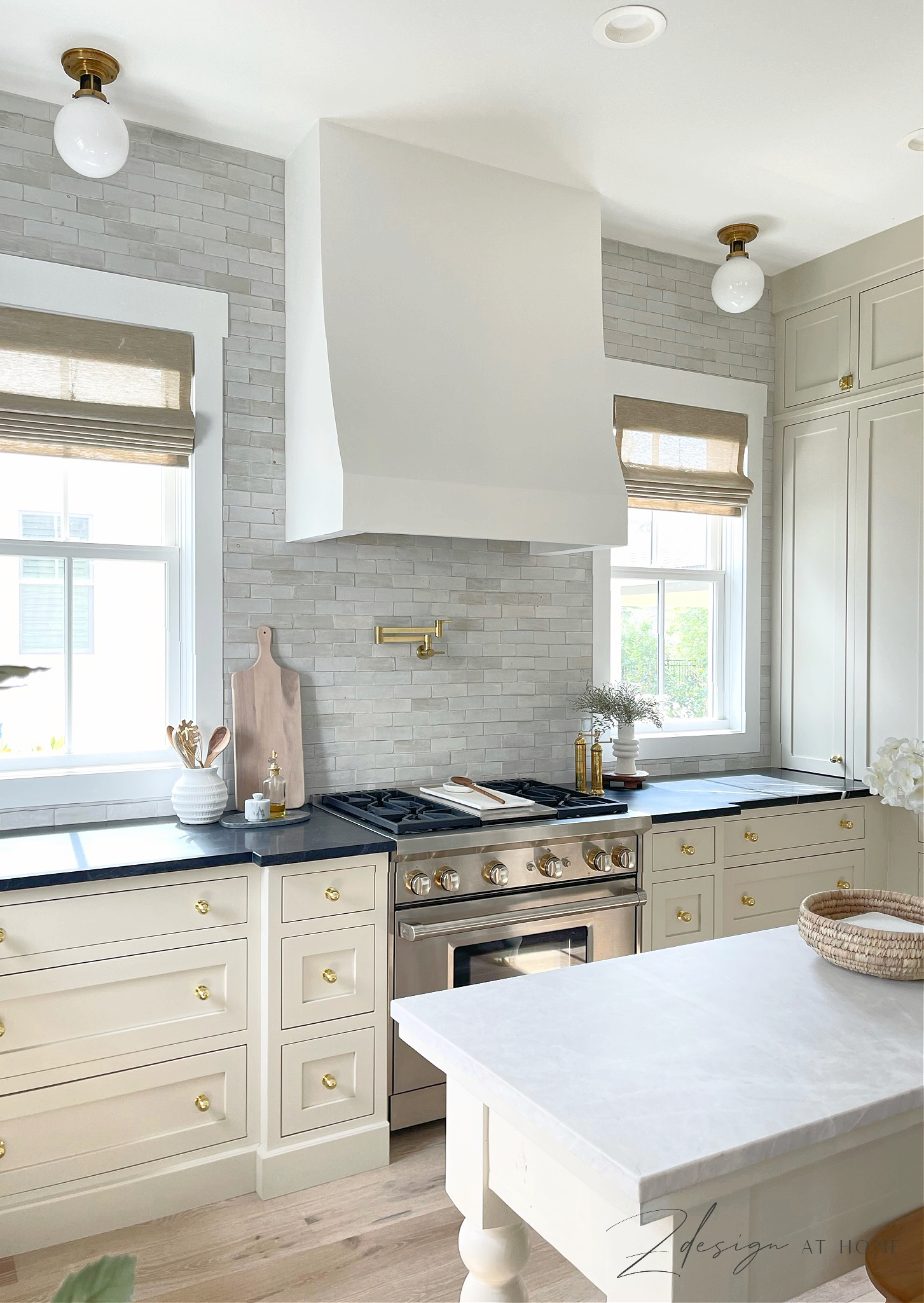 Natural cream cabinets and wolf range and french range hood in cottage kitchen with black marble countertops and zellige tile backsplash to ceiling 