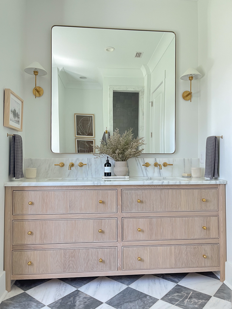 primary bath with fluted white oak vanity, marble checkered / harlequin patterned floors, oversized brass square mirror